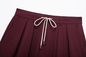 Detailed view of burgundy pleated trousers with adjustable beige drawstring waist tie