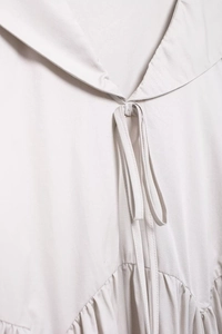 Détail du col en V avec nœud et plis à la taille sur robe midi élégante