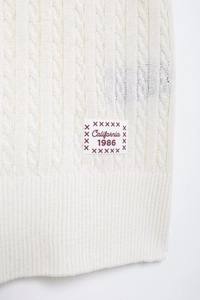 Detail of white cable knit texture and California 1986 patch on short sleeve polo top