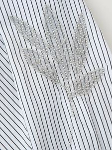 Detailed close-up of beaded leaf embroidery on white and black striped fabric