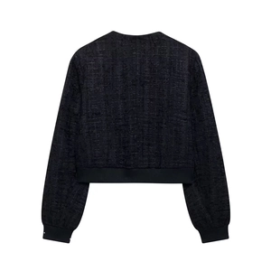 Détail de la texture de veste en tweed noir avec poignets en maille et coupe élégante