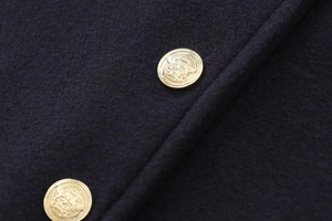 Detailed close-up of golden metal crest buttons on elegant navy wool jacket fabric