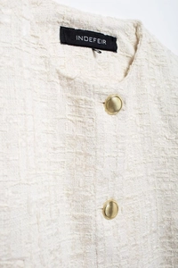 Détail de la texture tweed crème avec boutons dorés rayés élégants et encolure ronde