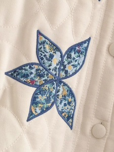 Detail of diamond quilted beige jacket featuring a blue floral flower applique and buttons