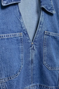 Detail of blue denim shirt showing v-neck collar, chest pockets and yellow stitching