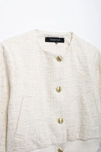 Détail d'une veste en tweed blanc avec tissage texturé et boutons dorés décoratifs en métal
