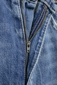Close-up of metal zipper and contrast stitching on mid-blue washed balloon jeans