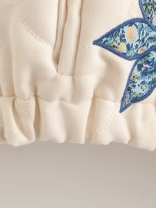 Detail of beige quilted jacket featuring floral leaf embroidery and elastic hemline