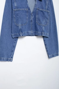 Detail of blue denim cropped jacket featuring large symmetrical pockets and premium stitching