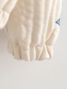 Detailed macro view of quilted cream fabric sleeve with elastic ribbed cuff and blue print