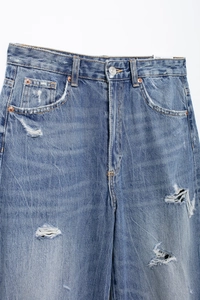 Detail of blue mid-rise jeans with distressed texture and vintage ripped accents