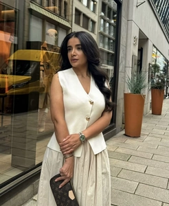 Close-up of white sleeveless knit vest with gold buttons and beige maxi skirt
