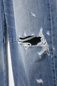 Detailed close-up of heavy distressed ripped design on light blue denim jeans