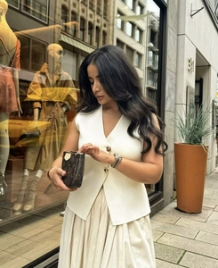 Detail of elegant cream V-neck knit vest and high-waist pleated maxi skirt set
