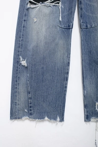 Detailed macro view of denim blue jeans showing distressed holes and raw hem design