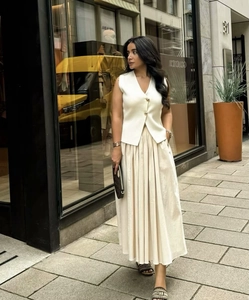 Detail of elegant cream v-neck knit vest with gold buttons and pleated maxi skirt
