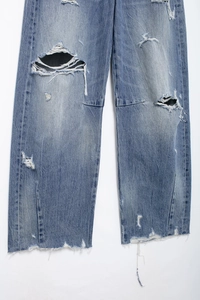 Detail of light blue distressed jeans showing ripped knee texture and frayed hem finish