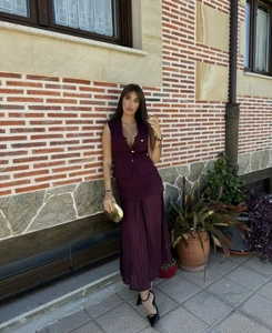 Detail of a dark purple sleeveless vest and pleated maxi skirt set in an outdoor setting