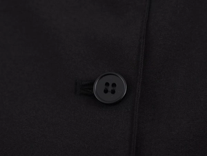 Close-up of a black four-hole resin button on a textured woven black dress fabric