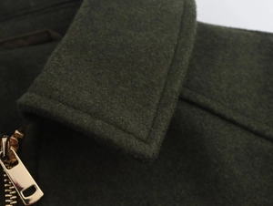 Gros plan sur la veste en laine vert foncé avec fermeture éclair dorée et coutures précises