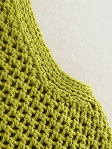 Primer plano del chaleco de punto verde hierba que muestra textura calada y borde acanalado