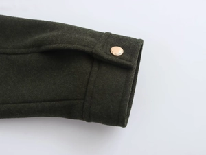 Détail du poignet d'une veste en laine vert foncé avec un bouton doré chic
