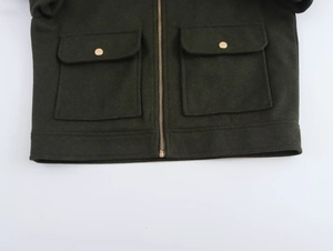 Détail d'une veste vert foncé avec fermeture éclair dorée et poches plaquées symétriques