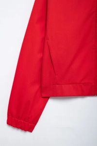 Detail of red zipper jacket showing twill fabric texture, elastic cuffs, and side pockets