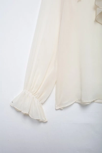 Detailed close-up of tiered ruffle collar and flared cuffs on a cream chiffon blouse