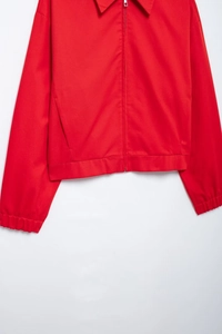 Detail shot of the red jacket featuring a metal zipper, classic collar, and woven fabric texture