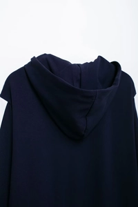 Detail of navy blue hoodie featuring a minimalist hood structure and white sleeve patchwork