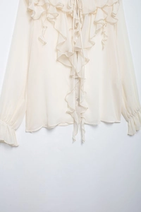 Close-up of ruffled layers and elegant bow tie on a cream-white long sleeve shirt