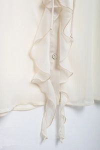 Detailed close-up of ruffle layers and round button on a beige chiffon shirt