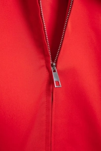 Detailed macro view of high-quality silver metal zipper on a red twill jacket