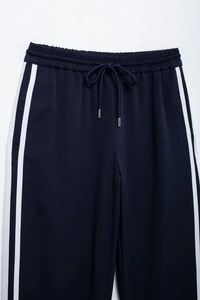 Detail of navy track pants featuring white side stripes and drawstring with metal tips