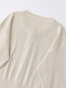 Detail shot of beige knit sweater showing ribbed crew neck and dropped shoulder seams