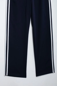 Detail of navy blue track pants featuring white side stripes and premium fabric texture