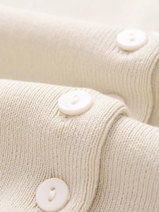 Close-up of beige knit fabric texture and white round buttons on street style sweater