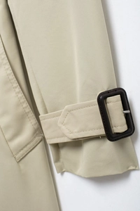 Detail shot of khaki trench coat sleeve featuring a cuff strap with a dark brown buckle