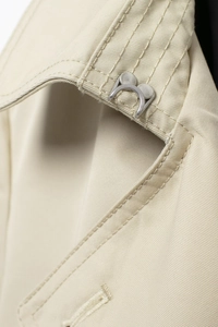 Macro detail of the silver metal hook fastening on a beige slim-fit trench coat neck
