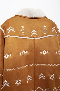 Detail of brown faux suede jacket featuring white floral embroidery and shearling collar