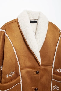 Close-up of white wavy embroidery on brown suede coat with cozy faux shearling trim
