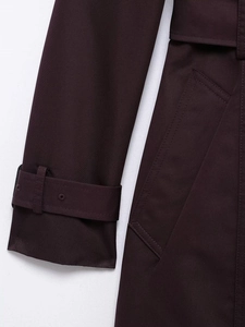 Detailed close-up of burgundy twill trench coat fabric with cuff straps and stitching