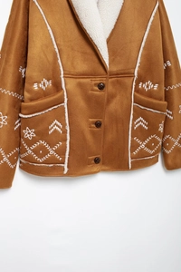 Detailed view of brown faux suede jacket with white shearling trim and floral embroidery