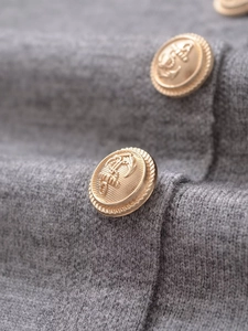 Detailed close-up of golden nautical anchor buttons on a gray knitted vest