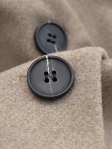 Close-up of black four-hole buttons with marble pattern on a light brown wool coat