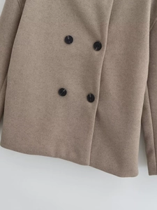 Macro detail of camel wool coat showing classic double-breasted buttons and soft fabric texture