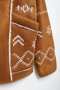 Detail of brown suede coat featuring white floral embroidery and soft shearling lining