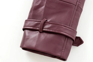 Close-up of burgundy leather jacket cuff with adjustable strap and refined stitching detail