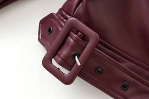 Detailed macro view of burgundy PU leather biker jacket belt buckle and metal grommets